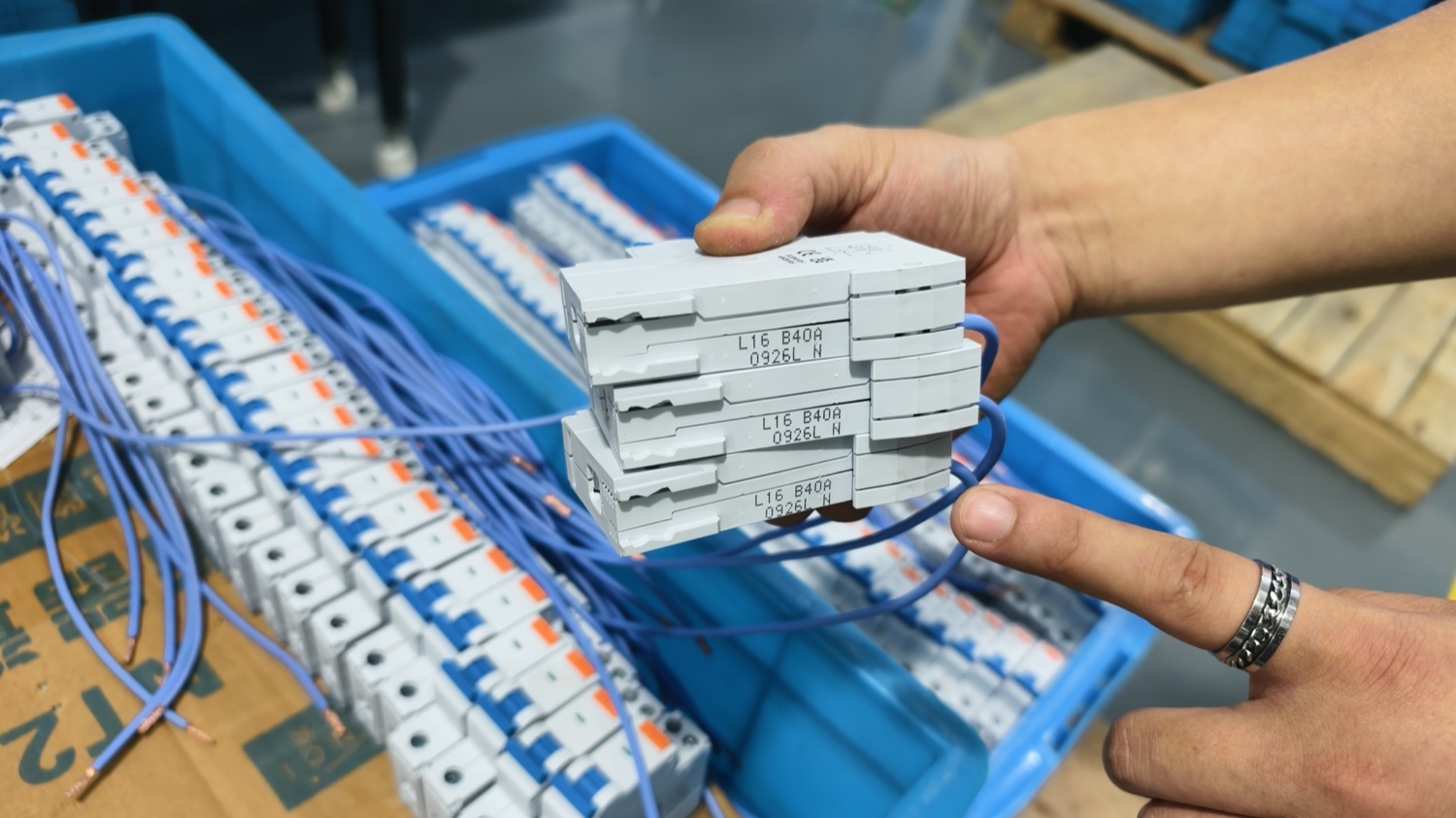 Assembled breakers being checked by hand against a tray of finished units